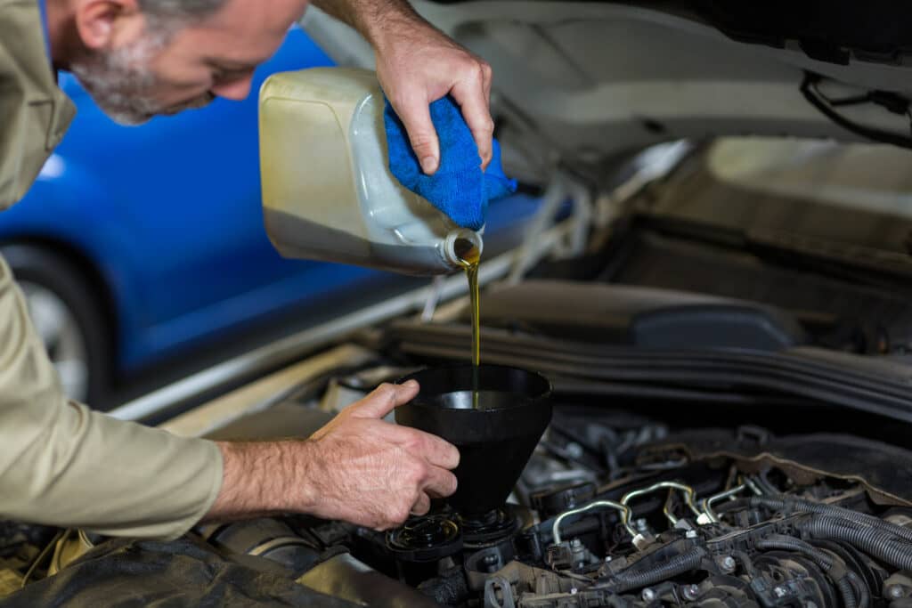 Mechanic pouring oil into car engine in repair garage